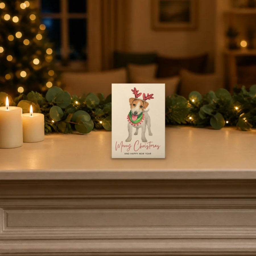 Jack Russell Christmas card standing on a festive mantelpiece with candles and garland, shown at its real 5 x 7 inch size