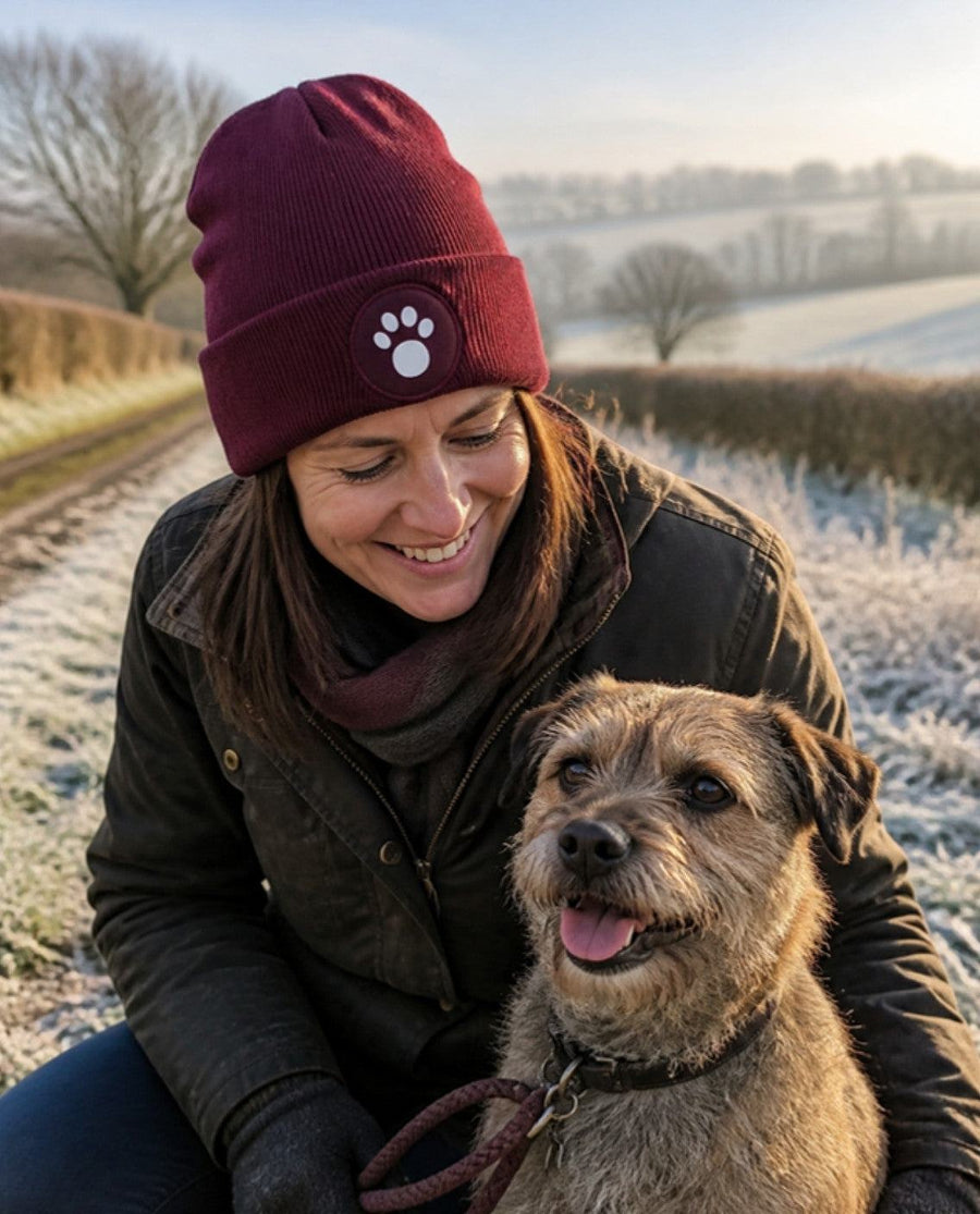 Woman wearing the burgundy Dog Paw Print Beanie Hat on a frosty walk with a Border Terrier