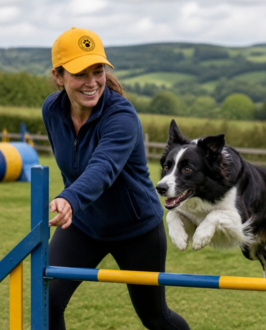 Woman in a yellow cap at dog agility with a Border Collie jumping