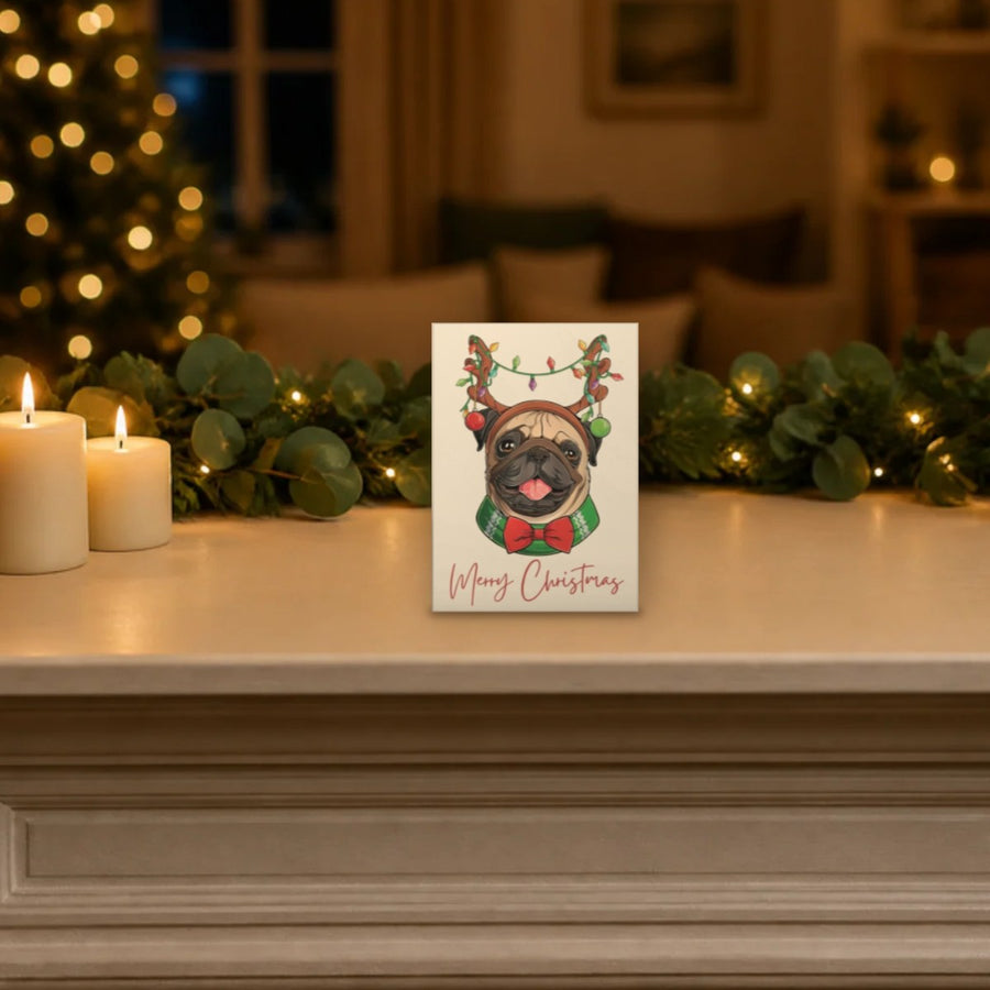 Pug Christmas card with fairy light antlers standing on a festive mantelpiece, shown at its real 5 x 7 inch size